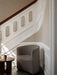 Tearoom Lounge Chair in patterned fabric, sitting in a sunlit corner next to an ornate white staircase and a wooden table.