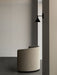 Side view of the beige Tearoom Lounge Chair in a minimalist space with a dark floor next to a black Cast Sconce Wall Lamp.