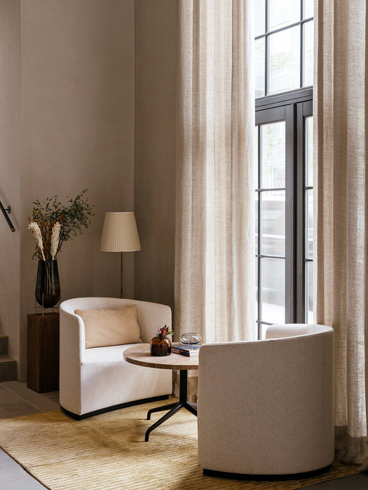 A living room setting with two off-white Tearoom Lounge Chairs and a Harbour Lounge Table on a textured rug next to a window.