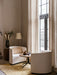 A living room setting with two off-white Tearoom Lounge Chairs and a Harbour Lounge Table on a textured rug next to a window.