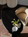 High-angle view of a beige bouclé Tearoom Lounge Chair beside a black coffee table with flowers and ceramics on a tile floor.