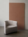 The Tearoom Lounge Chair in light grey upholstery, shown in a minimalist room with a concrete floor and a terracotta panel.