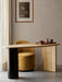 A yellow Tearoom Club Chair is tucked under the wooden Eclipse Desk in a softly lit, minimalist room with art on the wall.