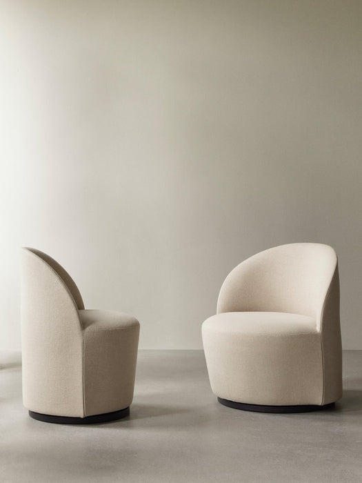 Two cream-coloured Tearoom Club Chairs with dark swivel bases in a minimalist room with concrete floors and a beige wall.