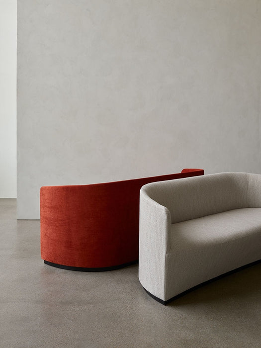 Two curved Tearoom Sofas, one in a light grey fabric and one in a burnt orange velvet, in a minimalist room.
