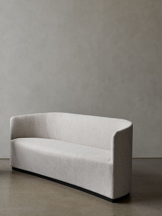 A three-quarter view of the Tearoom Sofa in a cream fabric, featuring a sculptural curved back and a recessed black base.