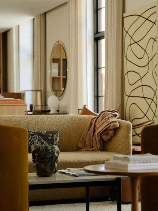 A light-coloured bouclé Tearoom Sofa in a styled living room with a coffee table, abstract art, and an oval mirror.