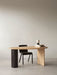 The asymmetrical Eclipse Desk in natural oak, styled with a black chair. On the desk sits a stack of books and a sculpture.