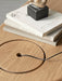A close-up of The Eclipse Desk in natural oak, showing the circular storage lid with a cable, books and a small sculpture.