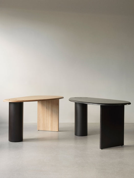 Two The Eclipse Desks, one in natural oak and one in black lacquered oak, shown side-by-side in a minimalist space.