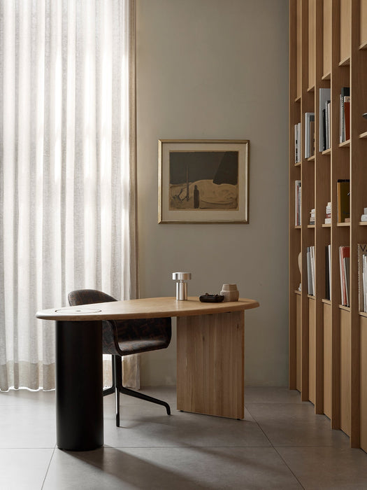 The Eclipse Desk in natural oak shown in a home office with a Harbour Dining Chair, a Column Table Lamp, and a bookcase.