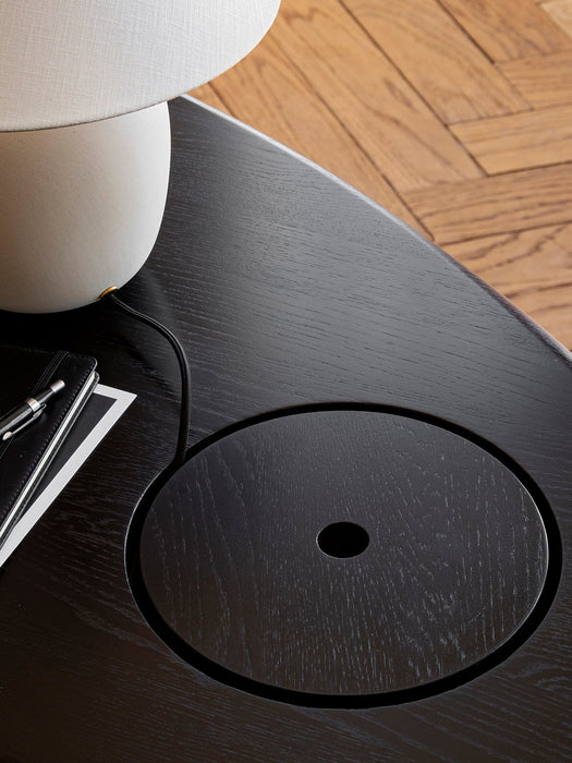 A close-up of The Eclipse Desk in black lacquered oak, showing the circular lid for hidden storage by a lamp and notebook.
