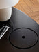 A close-up of The Eclipse Desk in black lacquered oak, showing the circular lid for hidden storage by a lamp and notebook.
