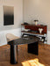 The black lacquered oak Eclipse Desk in a modern office with a beige chair, wooden shelving unit, and abstract wall art.
