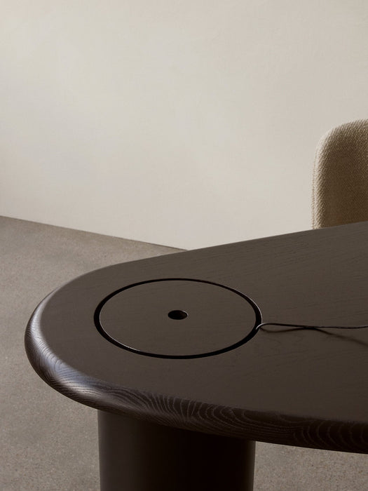 Close-up of The Eclipse Desk in black lacquered oak, showing the round storage lid, emerging cable, and curved tabletop.