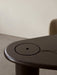Close-up of The Eclipse Desk in black lacquered oak, showing the round storage lid, emerging cable, and curved tabletop.