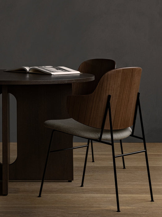 A Penguin Dining Chair with a walnut back and grey seat beside a dark wood Androgyne Dining Table with an open book.