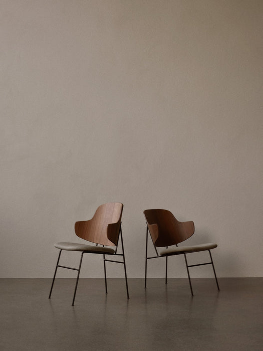 Two The Penguin Dining Chairs with sculpted walnut backrests and upholstered seats on thin black legs, set back-to-back.