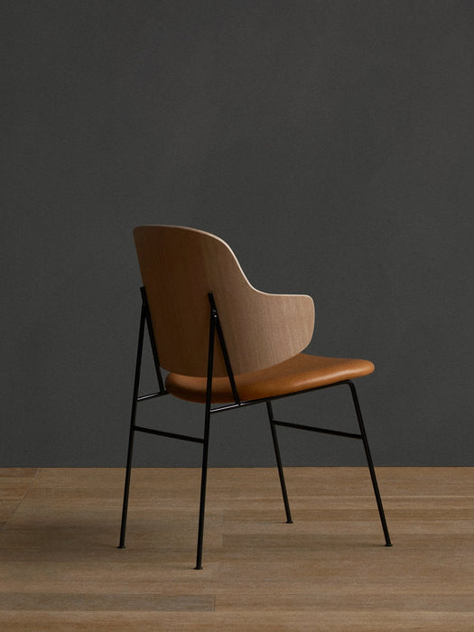 Rear three-quarter view of The Penguin Dining Chair with natural oak back, tan upholstered seat and slender black frame.