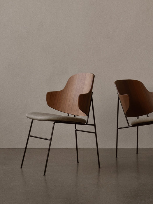 Two Penguin Lounge Chairs with iconic curved wooden backs and upholstered seats, set against a plain, neutral wall.
