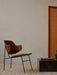 The Penguin Lounge Chair with a walnut back and light seat, placed on a striped rug next to a black marble plinth table.
