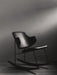 The black Penguin Rocking Chair, fully upholstered, seen from the side in a dark room with dramatic overhead lighting.
