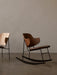 The Penguin Rocking Chair in walnut with a leather seat stands in a minimal room next to The Penguin Lounge Chair in oak.