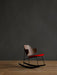 The Penguin Rocking Chair with a walnut backrest and red seat on a black frame, on a wooden floor against a dark wall.