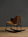 Three-quarter back view of The Penguin Rocking Chair with its walnut back, tan seat and black frame on a wood floor.