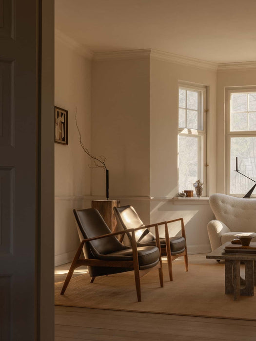 Two Seal Lounge Chairs in dark leather and a stone Androgyne Lounge Table arranged in a serene, sunlit living room.
