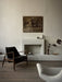Side view of The Seal Lounge Chair in black leather and dark wood, styled in a room with a fireplace and a grey Pagode Sofa.