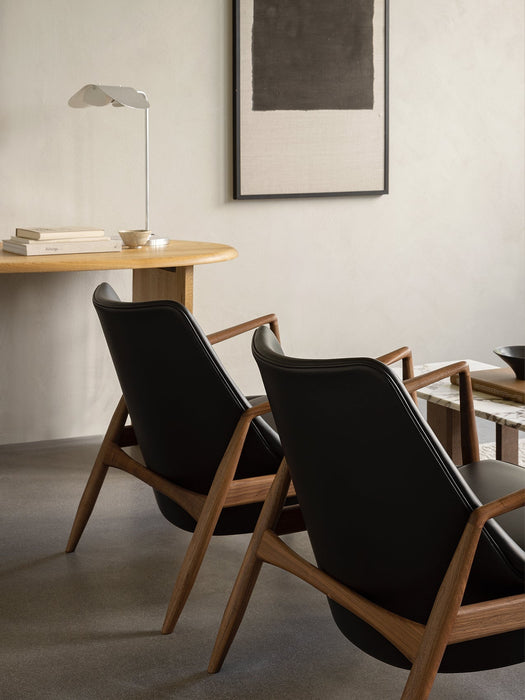 Rear view of two The Seal Lounge Chairs in walnut and black leather with an Eclipse Desk and Wing Table Lamp in background.