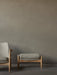 The Seal Ottoman in grey fabric and oak sits next to the Seal Lounge Chair on a dark wood floor against a taupe wall.