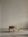 The Seal Ottoman with a natural oak frame and a thick, light brown cushion, shown in a minimalist room on a concrete floor.