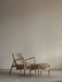 The Seal Lounge Chair and The Seal Ottoman, with light wood frames and beige fabric, in a minimalist room with grey floors.