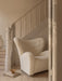 The Tired Man Lounge Chair in white boucle sits under a staircase. A Triptych Bowl rests on books on the light wood floor.