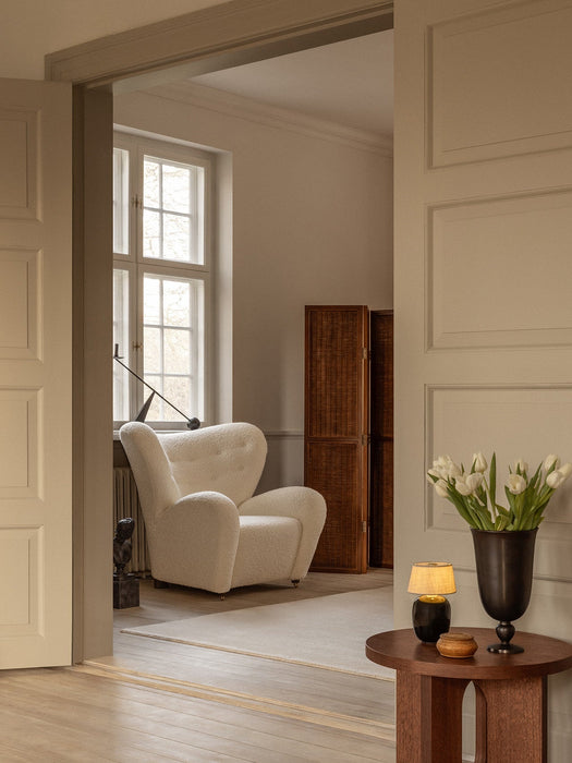 A white Tired Man Lounge Chair by a window. An Androgyne Side Table holds a Torso lamp and a Pavot Vase in the foreground.