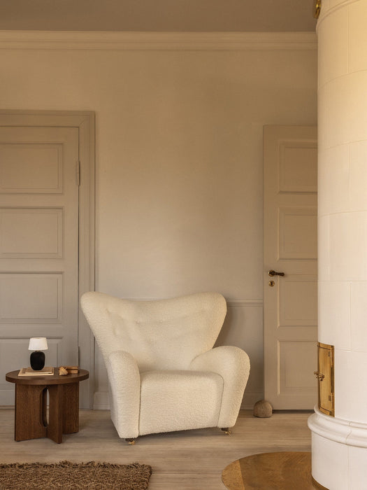 The Tired Man Lounge Chair in white bouclé sits by a dark oak Androgyne Side Table holding a Torso Portable Table Lamp.