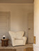 The Tired Man Lounge Chair in white bouclé sits by a dark oak Androgyne Side Table holding a Torso Portable Table Lamp.