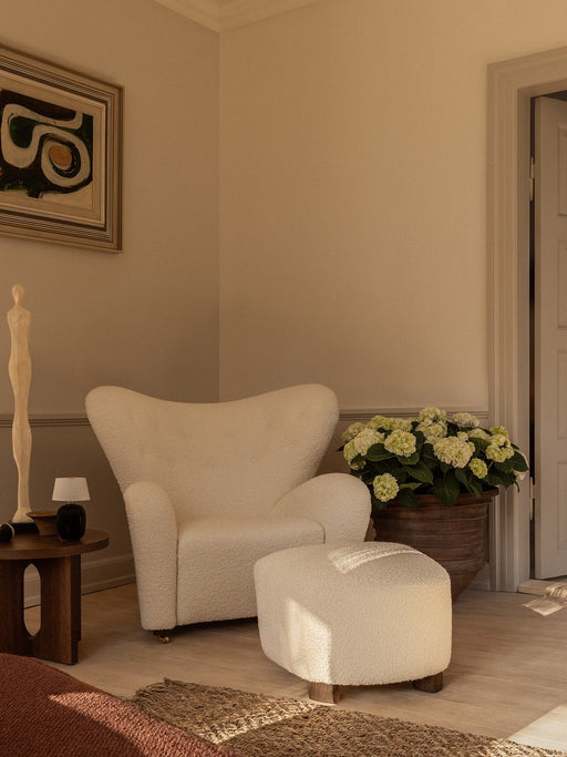 The Tired Man Lounge Chair & Ottoman in white bouclé, styled with an Androgyne Side Table, Torso Table Lamp & a potted plant.