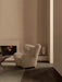 A beige Tired Man Lounge Chair in a minimalist room with a fireplace, coffee table, Kubus Vase, and a Hahira Lamp.