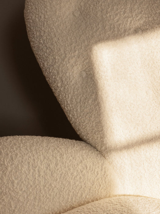A close-up of The Tired Man Lounge Chair, showing the soft, textured cream fabric with a geometric shadow cast on its curves.