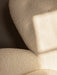 A close-up of The Tired Man Lounge Chair, showing the soft, textured cream fabric with a geometric shadow cast on its curves.
