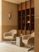 Two bouclé Harbour Lounge Chairs with a Volume Side Table on a Tile Rug. A Wing Wall Lamp hangs by a large wooden bookcase.