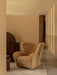 The Tired Man Lounge Chair in honey sheepskin sits on a Duomo Rug in a modern room with beige walls and dark wood furniture.