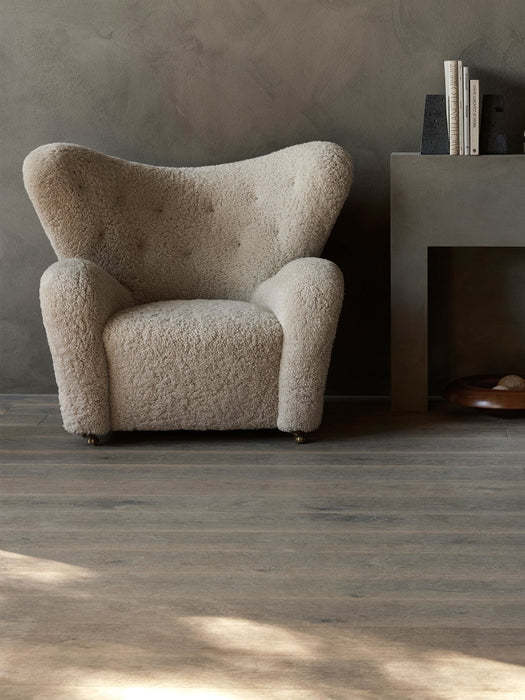 A fluffy, off-white The Tired Man Lounge Chair against a dark grey wall with Converge Book Ends and a Rond Bowl.