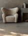 A fluffy, off-white The Tired Man Lounge Chair against a dark grey wall with Converge Book Ends and a Rond Bowl.