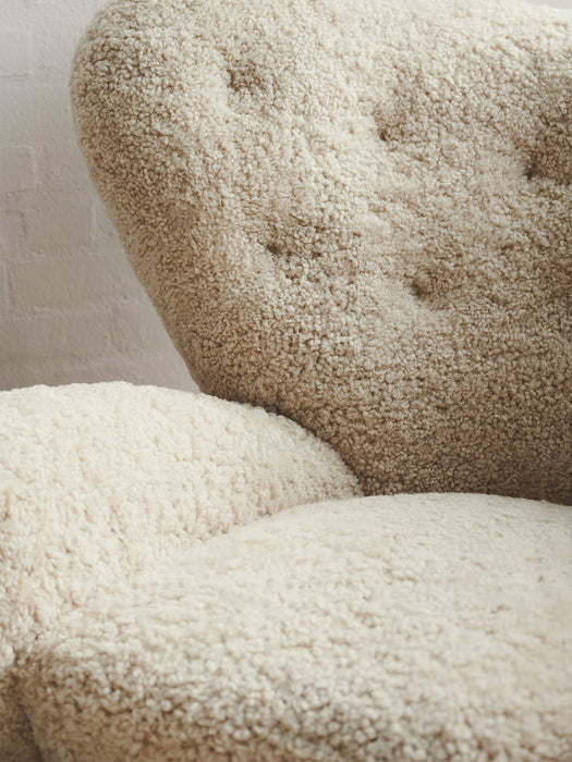 Close-up of The Tired Man Lounge Chair's plush, off-white sheepskin upholstery, detailing the tufted backrest and soft seat.