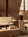A cosy, brown-toned living room with a Torso Table Lamp on a marble Plinth, beside a cream Brasilia Sofa and Lounge Chair.