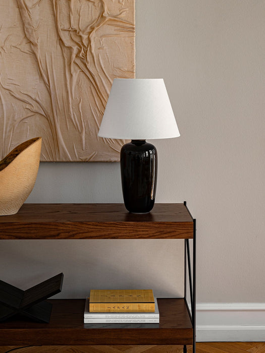 The Torso Table Lamp, 57, styled on a dark wood console table with books, a decorative bowl, and textured wall art behind it.